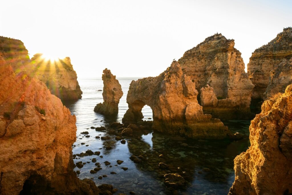 The sun shines through the rocks near the ocean